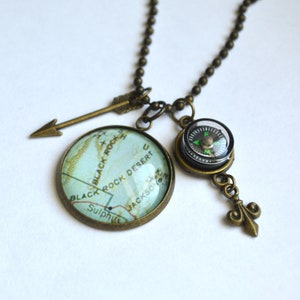 May include: A bronze necklace with a compass, arrow, and a glass cabochon featuring a map of Black Rock Desert. The map shows the words "Black Rock Desert", "Black Rock", "Sulphur", and "Jackson".