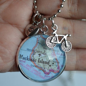 Op de afbeelding: Een zilveren ketting met een bedel met een kaart van Mackinac Island, Michigan. De bedel bevat ook een klein hartje en een fietsbedel.