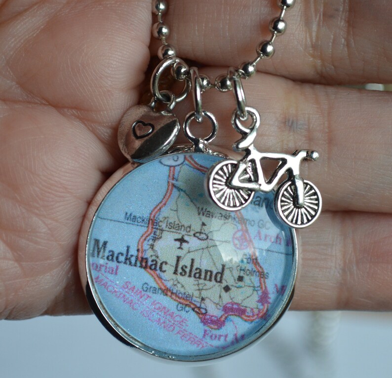 Op de afbeelding: Een zilveren ketting met een bedel met een kaart van Mackinac Island, Michigan. De bedel bevat ook een klein hartje en een fietsbedel.