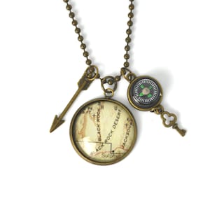 May include: A bronze necklace with a compass, a key charm, and a round pendant featuring a map of Black Rock Desert, Nevada. The pendant has the text "Black Rock Desert" and "Sulphur" on it.