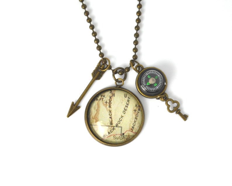 May include: A bronze necklace with a compass, a key charm, and a round pendant featuring a map of Black Rock Desert, Nevada. The pendant has the text "Black Rock Desert" and "Sulphur" on it.