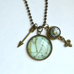 May include: A bronze necklace with a compass, arrow, and a glass pendant featuring a map of Black Rock Desert, Nevada. The map shows the words "Black Rock Desert", "Sulphur", and "Jackson".