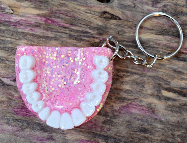 K&ouml;nnte beinhalten: Rosa glitzernder Schl&uuml;sselanh&auml;nger aus Harz in Form eines Gebisses mit wei&szlig;en Z&auml;hnen.