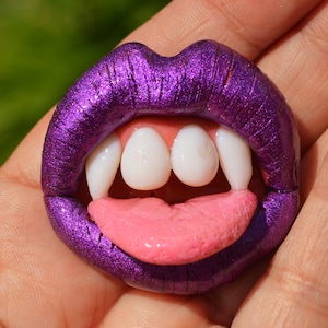 May include: A purple glitter lip ring with a set of white vampire teeth and a pink tongue.