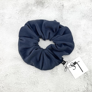 Peut inclure: Un chouchou en velours côtelé bleu marine avec une étiquette attachée. Le chouchou est circulaire et présente une texture côtelée. L'étiquette est blanche avec les lettres "ST" en noir.