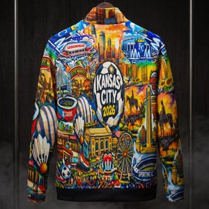 Puede incluir: Chaqueta bomber colorida con un collage vibrante de im&aacute;genes de Kansas City. El dise&ntilde;o incluye un bal&oacute;n de f&uacute;tbol con el texto "Kansas City 2026", paisajes urbanos e iconos. La chaqueta tiene cuello y pu&ntilde;os negros.