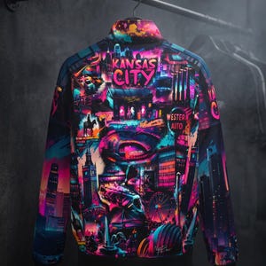 May include: A vibrant bomber jacket featuring a colorful graphic of Kansas City landmarks. The design includes the city's skyline, Ferris wheel, and the words "Kansas City" in bright pink. The jacket is hanging on a metal rack.