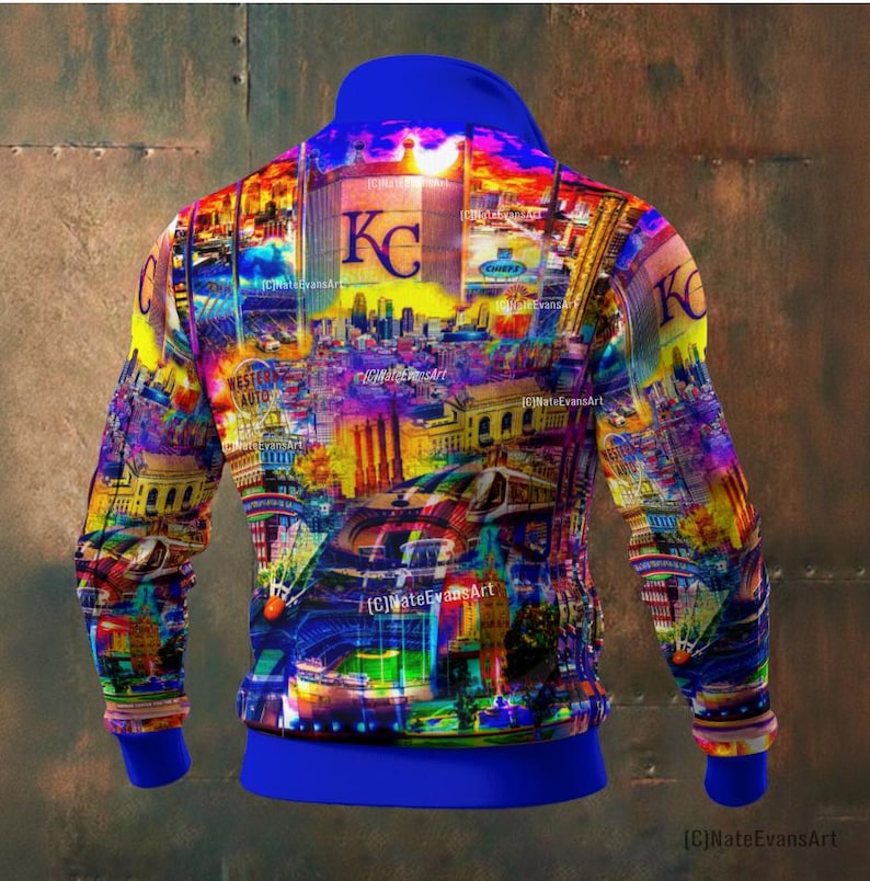 May include: A vibrant, colorful zip-up hoodie featuring a cityscape design with the letters "KC" prominently displayed. The design incorporates a variety of colors, including blue, yellow, and purple. The hoodie has a blue collar, cuffs, and waistband.
