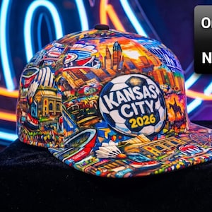 May include: A colorful baseball cap featuring a collage of Kansas City landmarks and the text "Kansas City 2026" on a soccer ball emblem. The cap's design includes buildings, a Ferris wheel, and other city elements.