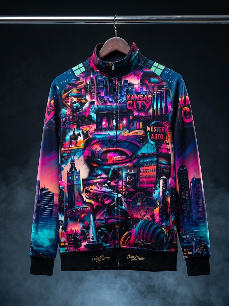 May include: A zip-up jacket with a vibrant, colorful design featuring a cityscape with the text "Kansas City" and "Western Auto". The jacket has a black collar, cuffs, and hem, and is hanging on a wooden hanger.