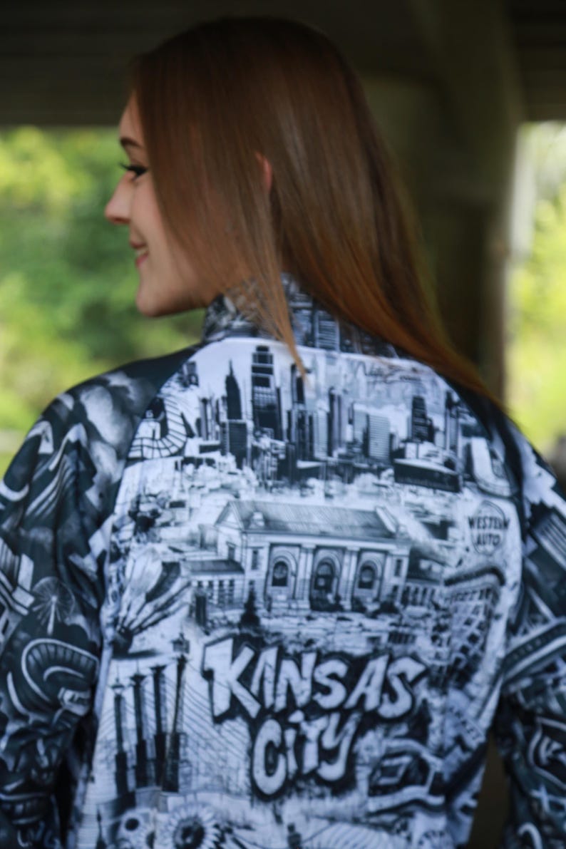 May include: A black and white jacket featuring a detailed graphic of the Kansas City skyline and the city's name in bold lettering. The jacket's design includes iconic landmarks and architectural elements.