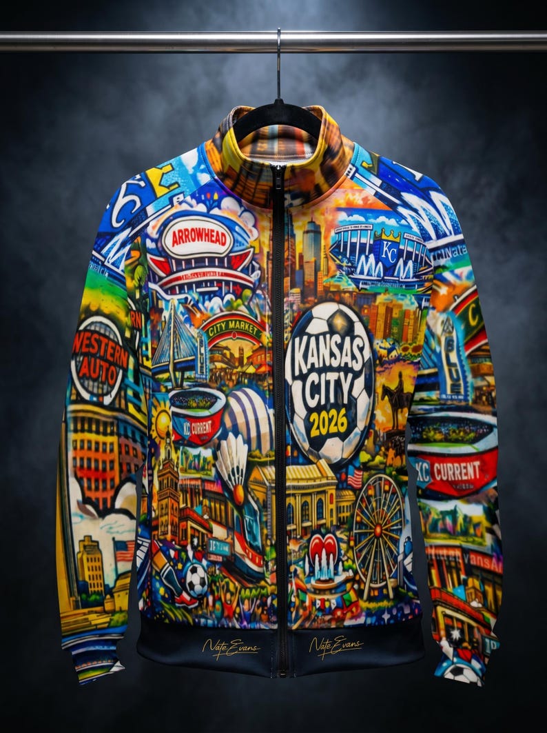 Puede incluir: Chaqueta con cremallera multicolor con un collage vibrante de los lugares emblem&aacute;ticos de Kansas City y el texto "KANSAS CITY 2026". El dise&ntilde;o incluye im&aacute;genes del estadio Arrowhead, City Market y un bal&oacute;n de f&uacute;tbol. La chaqueta est&aacute; colgada en una percha negra.