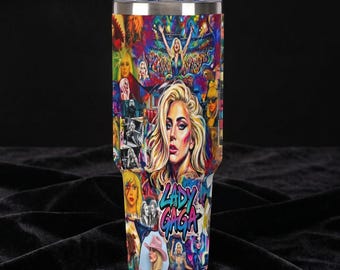 May include: A stainless steel tumbler featuring a vibrant collage of images of Lady Gaga. The design includes portraits, concert scenes, and the artist's name in a stylized font. The tumbler has a clear lid.