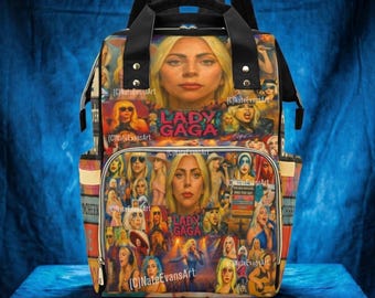May include: A multi-colored backpack featuring a collage of images of Lady Gaga. The design includes various portraits and performance shots of the artist, with the text "LADY GAGA" prominently displayed. The bag has black straps and a top handle.