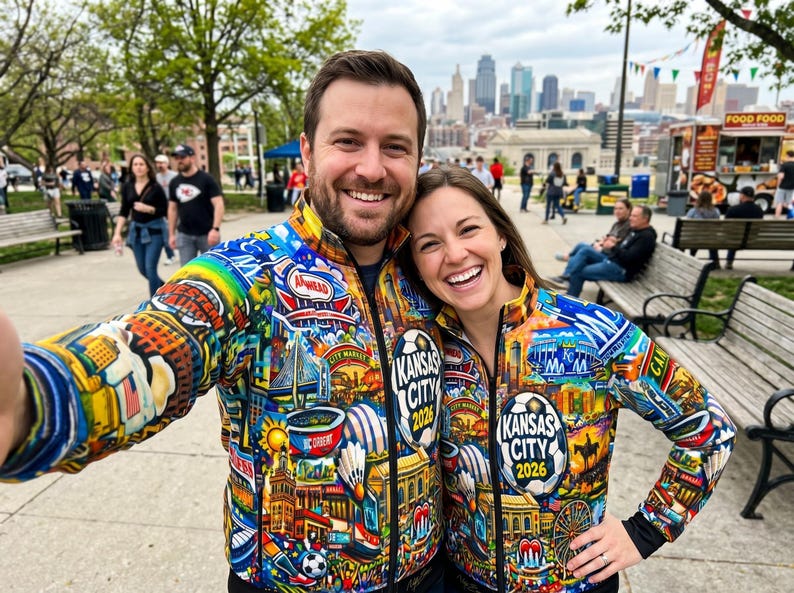 Puede incluir: Una pareja sonr&iacute;e, vistiendo chaquetas con cremallera a juego con ilustraciones coloridas de los lugares emblem&aacute;ticos de Kansas City y el texto "Kansas City 2026". Las chaquetas presentan un dise&ntilde;o de arco&iacute;ris e iconos de la ciudad.
