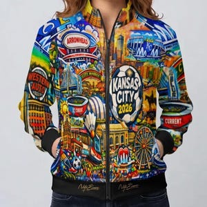 Puede incluir: Chaqueta bomber con cremallera con un dise&ntilde;o vibrante y colorido que presenta los puntos de referencia de Kansas City y el texto "Kansas City 2026". La chaqueta tiene cuello, pu&ntilde;os y dobladillo negros, y la firma del artista es visible.