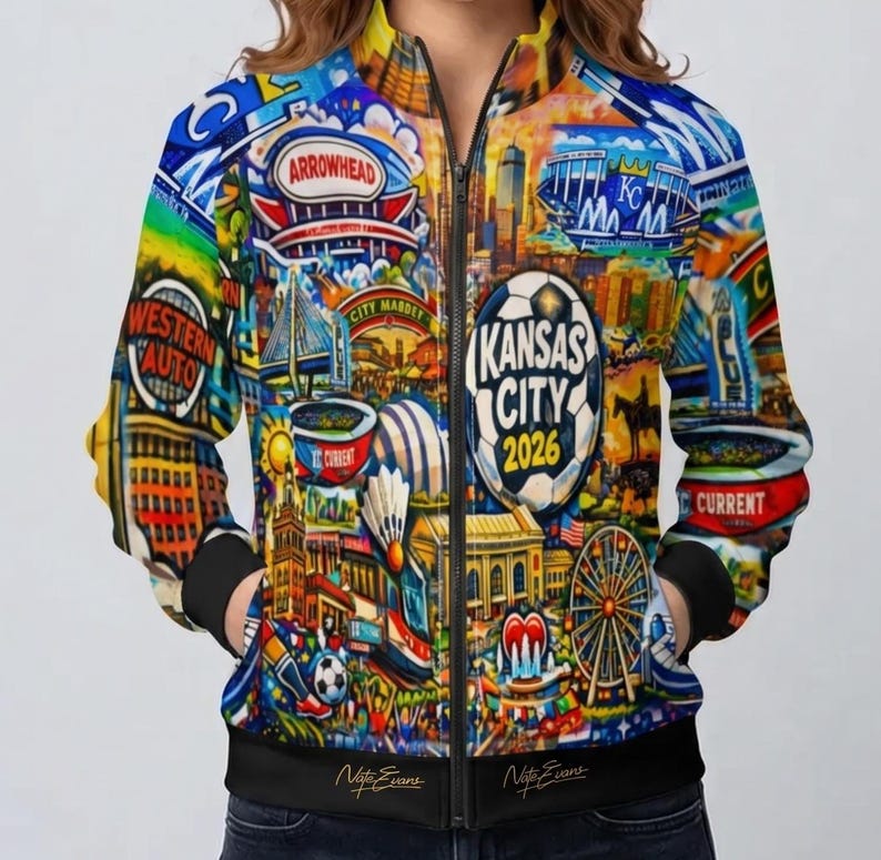 Puede incluir: Chaqueta bomber con cremallera con un dise&ntilde;o vibrante y colorido que presenta los puntos de referencia de Kansas City y el texto "Kansas City 2026". La chaqueta tiene cuello, pu&ntilde;os y dobladillo negros, y la firma del artista es visible.