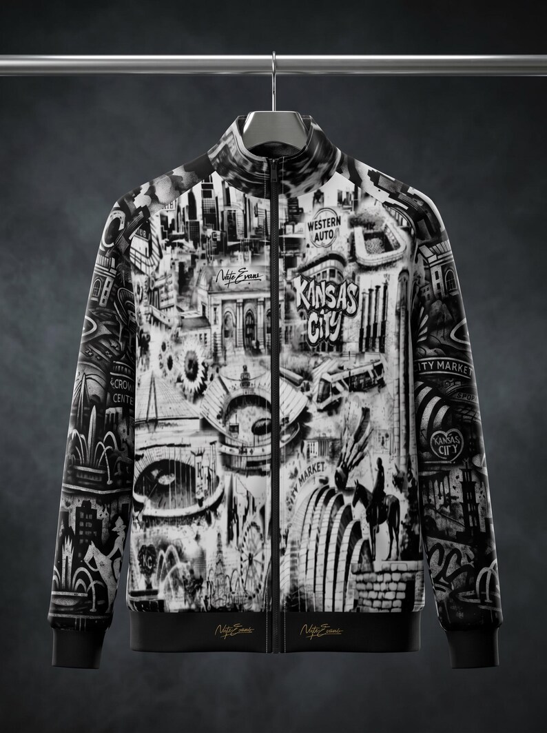 May include: Black and white zip-up jacket featuring a detailed graphic of Kansas City landmarks and the text "Kansas City". The jacket has a stand-up collar, black trim, and the signature "Nate Evans" on the bottom.