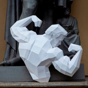 Può includere: Una scultura di carta bianca di una figura muscolosa con le braccia flesse, in piedi davanti a una statua grigio scuro.
