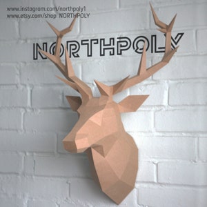 May include: A brown papercraft deer head mounted on a white brick wall. The deer has large antlers and a detailed face. The text "NORTHPOLY" is printed above the deer head.