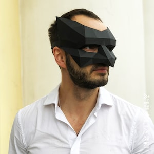 May include: A black origami mask with a geometric design. The mask covers the eyes and nose and has a pointed shape at the top.
