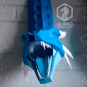 May include: A blue papercraft dragon head with white teeth and spikes. The dragon's mouth is open and its eyes are closed. The dragon is mounted on a wall. The text "GURKO DESIGN STUDIO" is visible in the upper right corner of the image.