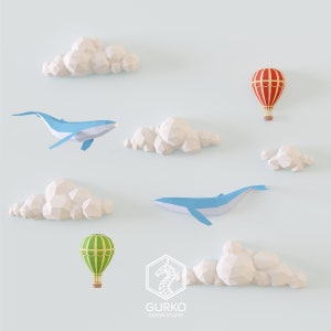 Puede incluir: Una ilustración digital de una ballena azul, dos globos aerostáticos, uno rojo y otro verde, y nubes blancas sobre un fondo azul claro. El texto "GURKO DESIGN STUDIO" está en la parte inferior de la imagen.