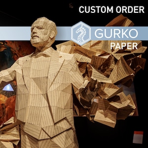 Puede incluir: Una escultura de papel de una persona hecha de hojas de papel de música. La escultura está de pie en una habitación oscura con un cartel azul y blanco encima que dice "CUSTOM ORDER GURKO PAPER".