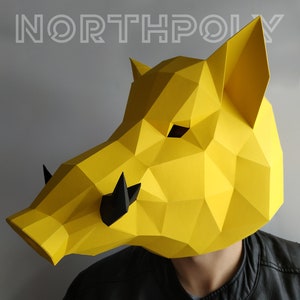May include: A yellow papercraft mask of a boar's head with black details. The mask is made of folded paper and has a three-dimensional effect.