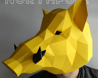 May include: A yellow papercraft mask of a boar's head with black details. The mask is made of folded paper and has a three-dimensional effect.