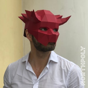 May include: A red papercraft mask with horns, resembling a demon or devil. The mask is made of folded paper and has a geometric design.
