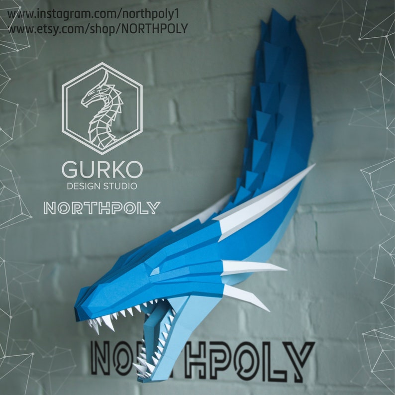 May include: A blue papercraft dragon head with white accents, mounted on a brick wall. The dragon has a wide open mouth with sharp teeth. The text "NORTHPOLY" is visible in the image.