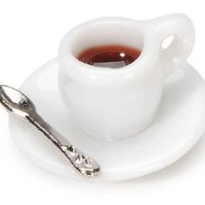May include: Miniature white ceramic teacup filled with a dark liquid, resting on a matching saucer. A small silver spoon is placed to the side. The set is designed for a dollhouse or miniature display.