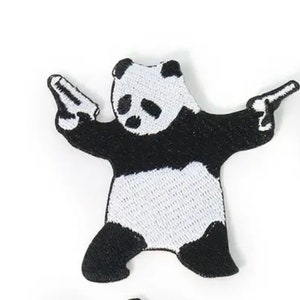 May include: Embroidered patch featuring a black and white panda holding two toy guns. The panda is in a standing pose with its arms outstretched, and the guns are pointed outwards. The patch has a detailed, stitched design.