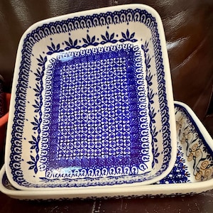 May include: A rectangular ceramic baking dish featuring a white base with a dense blue floral pattern in the center, surrounded by a border of blue stylized leaves and swirls. A second, larger matching rectangular dish sits underneath it.