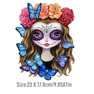 Peut inclure: Une illustration colorée d'une fille avec un visage de sucre crâne portant une couronne de fleurs avec des papillons bleus. Le texte "Taille : 23 X 17,8 cm/9,05 X 7 pouces" est en bas de l'image.
