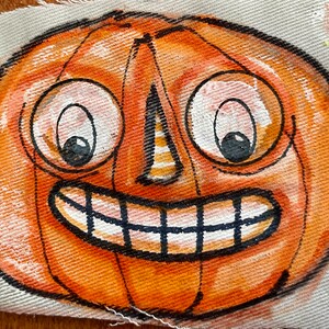 May include: A hand-painted orange pumpkin with a wide, toothy grin and large, round eyes. The pumpkin is painted on a white canvas.