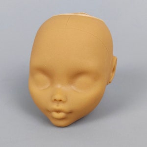 May include: A tan-colored doll head with closed eyes, a small nose, and full lips. The head has a smooth texture and is designed with a neutral expression. The doll head is a craft supply for doll making.