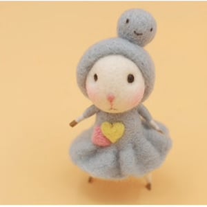 May include: A small, gray felt animal with a heart-shaped patch on its chest. The animal has a round head with a small, smiling face and a gray felt hat.