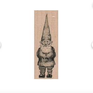 May include: A wood-mounted rubber stamp featuring a detailed illustration of a garden gnome. The gnome is depicted with a long, pointed hat, a full beard, and a belted tunic. The stamp is ideal for crafting and scrapbooking projects.