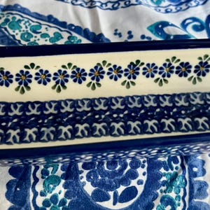 May include: A rectangular ceramic serving dish with a blue floral design. The dish has a cream-colored interior with blue and green floral patterns along the edges and a central blue design. The rim and exterior are dark blue.