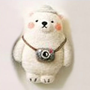 May include: A charming white polar bear ornament, complete with a grey hat and a camera slung around its neck. The bear has rosy cheeks and black eyes. The camera is grey with a black lens and a red detail. A whimsical, handcrafted item.
