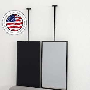 Pode incluir: Dois espelhos retangulares, um preto e outro com superfície refletora, suspensos no teto por hastes pretas. Os espelhos são emoldurados em preto. Um gráfico circular com uma bandeira americana e texto é visível.