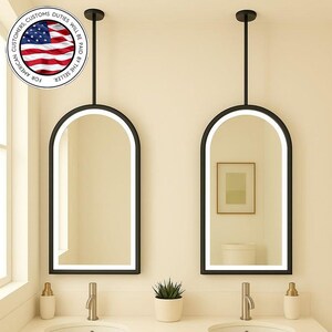 May include: Two arched, black-framed mirrors with integrated LED lighting hang above a double vanity. The vanity features two sinks, faucets, and a small potted plant. The text in the image says "FOR AMERICAN CUSTOMERS, CUSTOMS DUTIES WILL BE PAID BY THE SELLER."