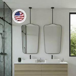 Pode incluir: Design moderno de casa de banho com uma bancada de madeira flutuante com duas pias retangulares brancas e torneiras pretas. Dois espelhos únicos com moldura preta penduram-se por cima. Uma cabine de duche de vidro e uma janela com vegetação são visíveis.