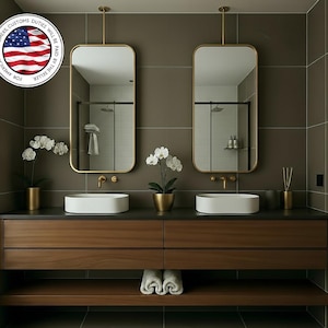 Pode incluir: Um design de casa de banho moderno com dois espelhos retangulares com moldura dourada suspensos sobre uma bancada de madeira escura com duas pias brancas. A bancada tem gavetas e uma prateleira inferior com toalhas dobradas. Detalhes dourados decorativos e orquídeas em vasos.