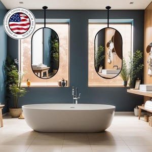 May include: A modern bathroom with a white oval bathtub, two black-framed oval mirrors, and wooden accents. The room features a large window, plants, and a wooden bench with towels. The overall design is minimalist and spa-like.