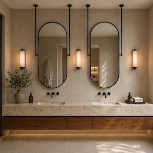 May include: A double vanity bathroom featuring a long marble countertop with two integrated sinks, matte black faucets, and two oval mirrors suspended from the ceiling by black rods. Three vertical wall sconces provide warm lighting.