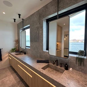 K&ouml;nnte beinhalten: Ein modernes Badezimmer mit zwei Waschbecken, einem gro&szlig;en Fenster mit Blick auf das Wasser und einem schwebenden Waschtisch mit Holzschr&auml;nken.