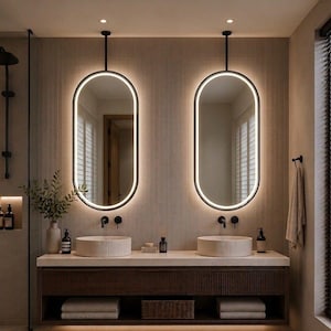 Puede incluir: Dos espejos de pared ovalados con retroiluminaci&oacute;n LED integrada, suspendidos del techo mediante varillas de metal negro. Los espejos se sit&uacute;an sobre un mueble de ba&ntilde;o doble con dos lavabos redondos de cer&aacute;mica estriada.